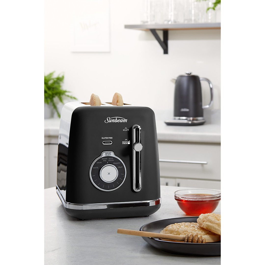 Black 2-slice toaster with bread in a kitchen setting with honey and kettle
