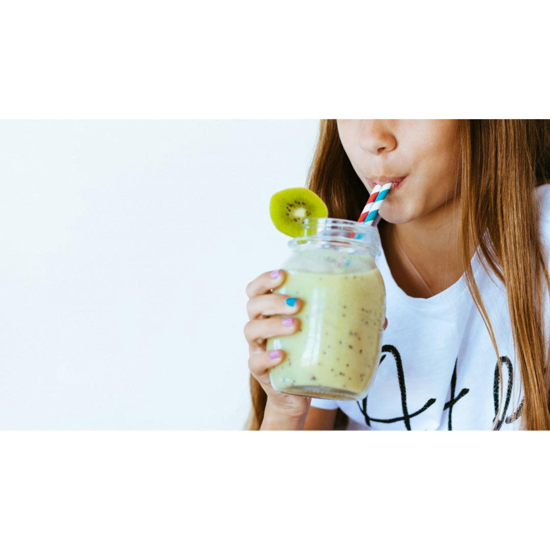 Young person drinking a kiwi smoothie from a blender jar with a straw