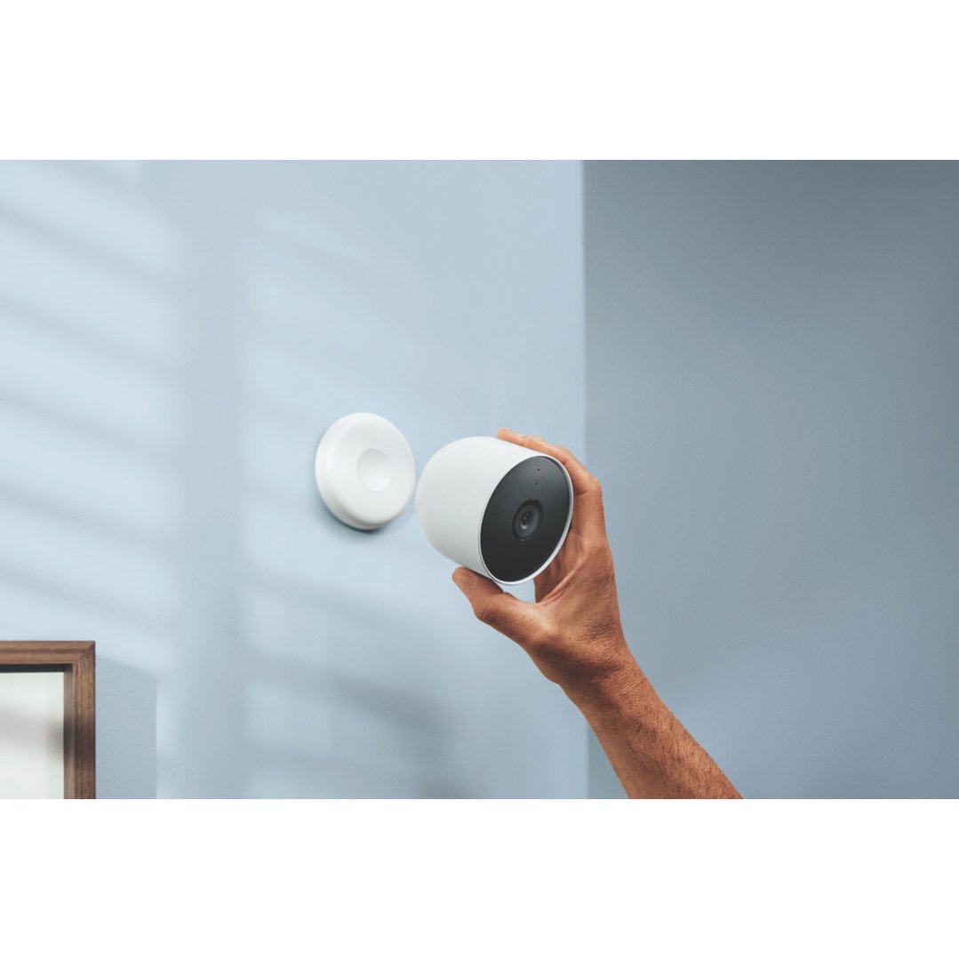 A hand holding a white security camera next to its wall mount