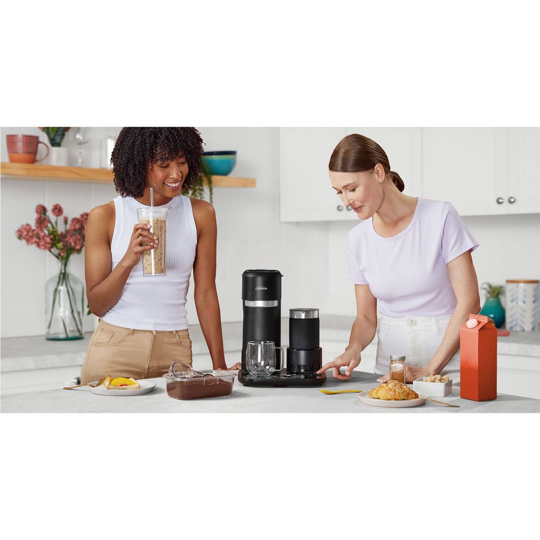 Two women preparing coffee and breakfast with a coffee machine on a counter