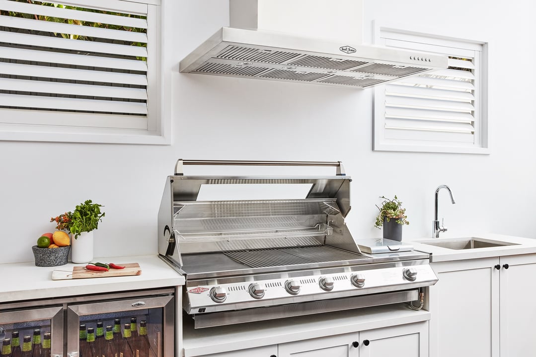Stainless steel rangehood mounted above a grill in an outdoor kitchen setting