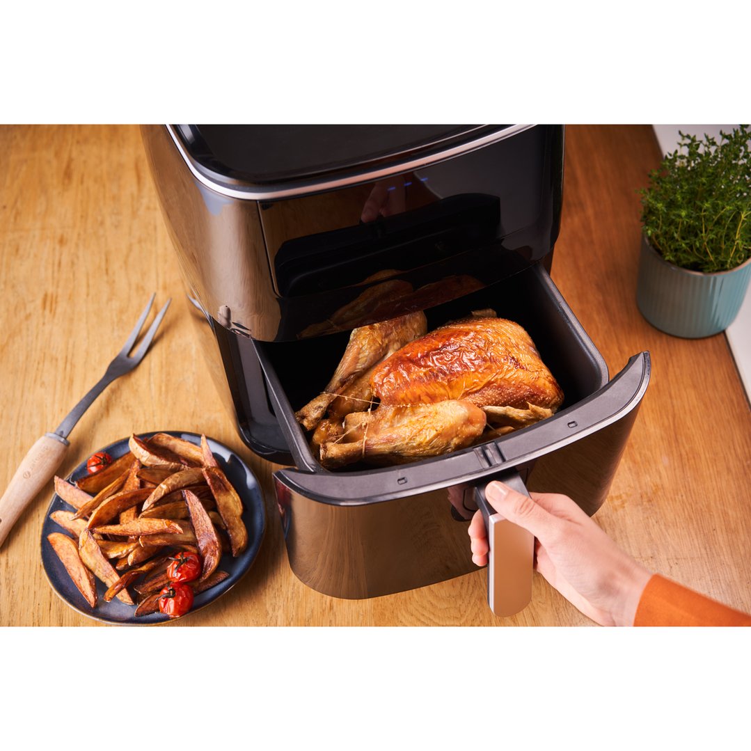 Hand pulling out air fryer basket with whole chicken and fries