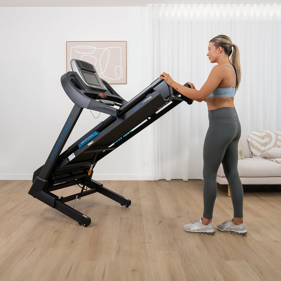 Woman folding a black treadmill in a bright room with wooden floors