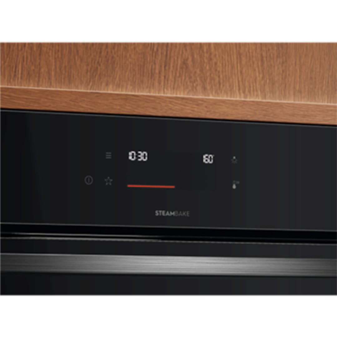 Close up of an oven's black control panel with digital display and wooden cabinetry
