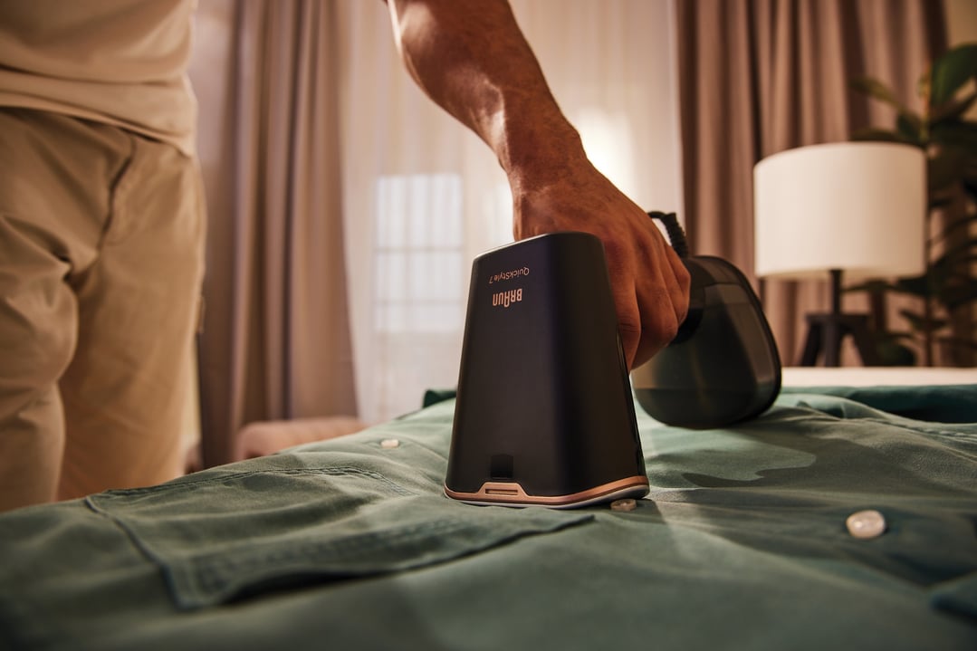 Man's hand using a Braun QuickStyle 7 Garment Steamer on a green shirt