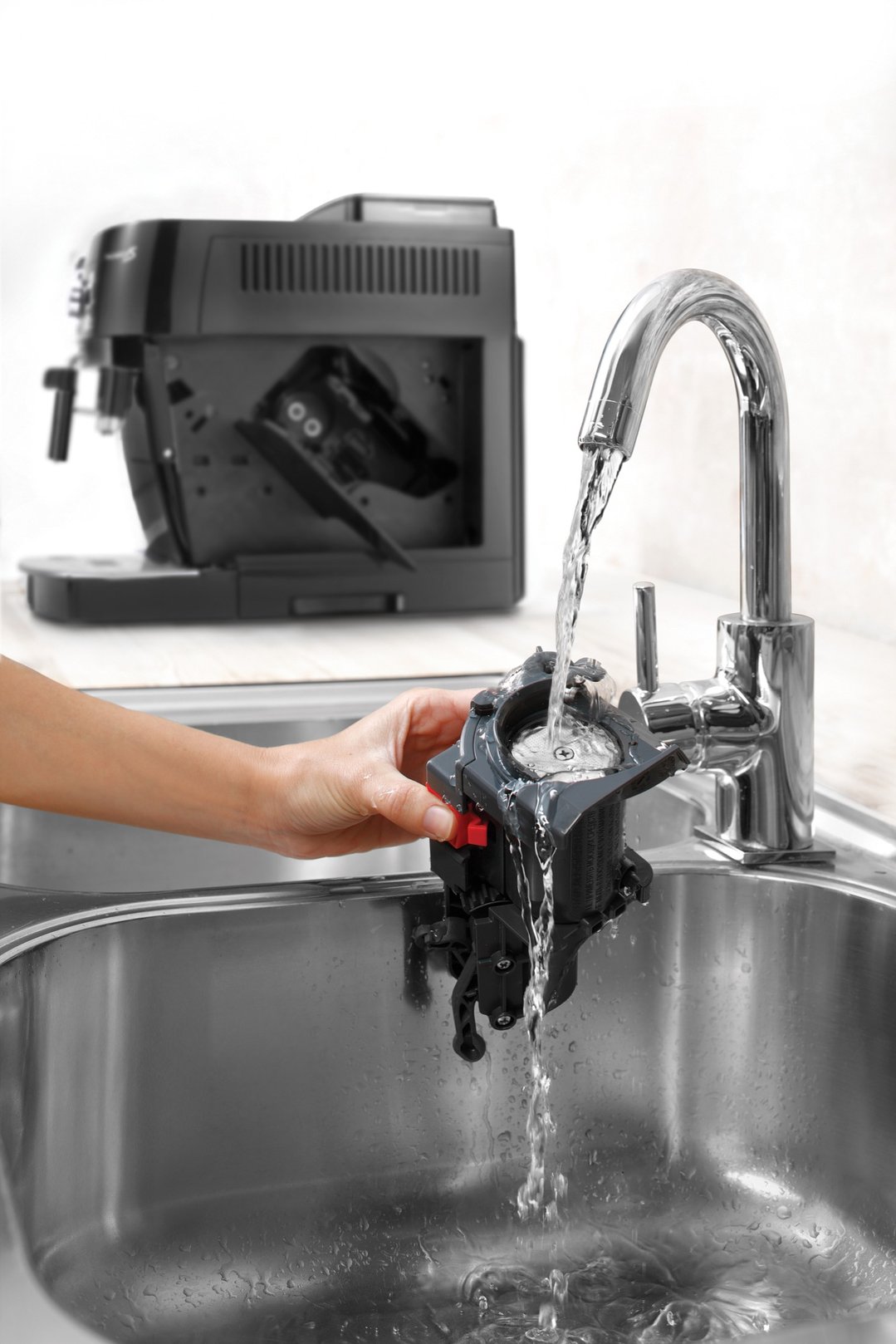Hand washing a component of a coffee machine under a running tap in a sink