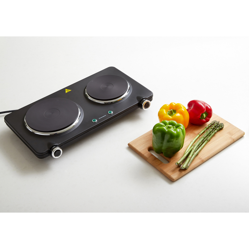 Black double electric hotplate on a white counter with vegetables