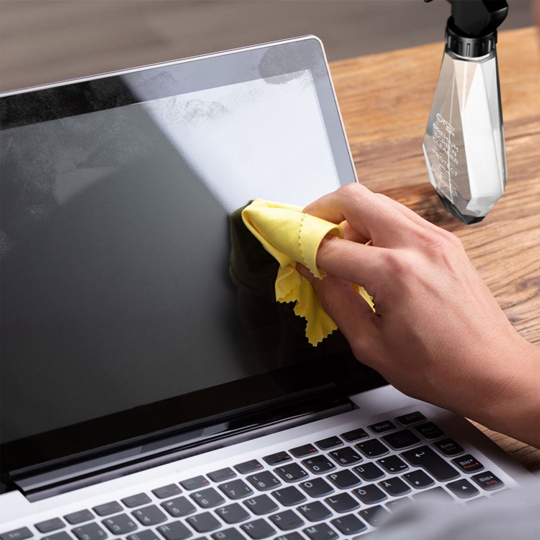 Hand cleaning a laptop screen with a yellow cloth and screen cleaner