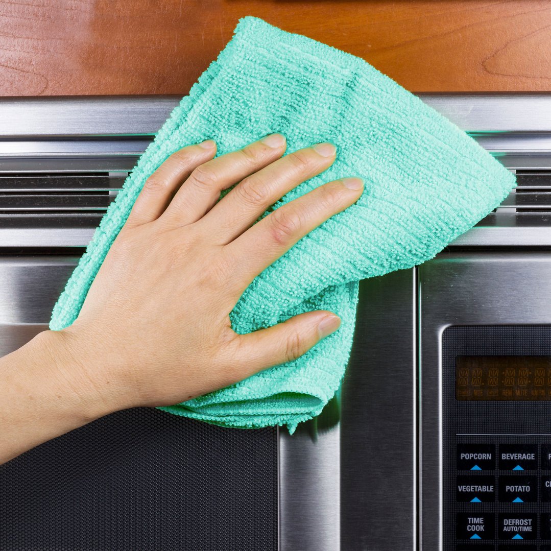 Hand wiping down a stainless steel microwave with a turquoise cleaning cloth