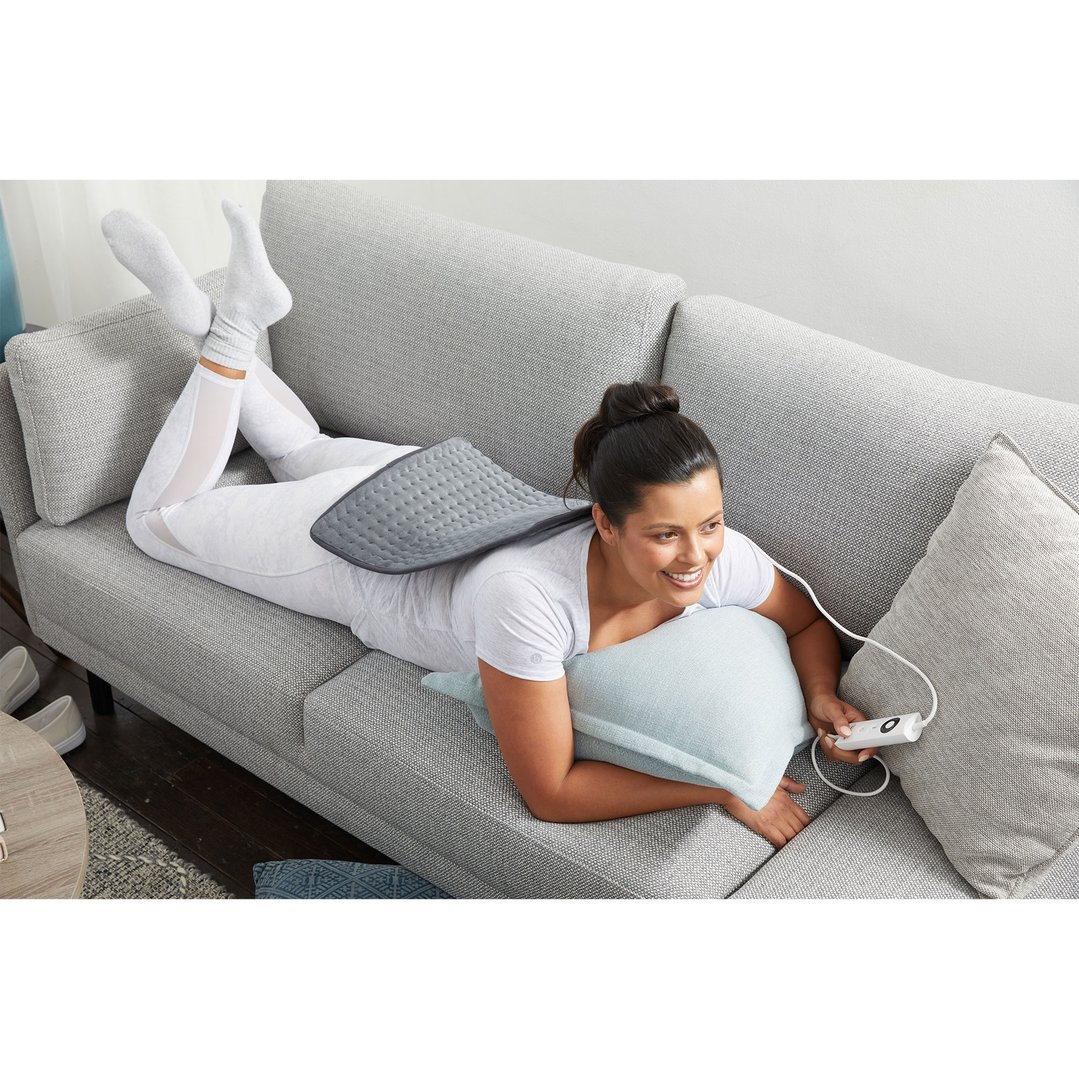 Woman lying on a sofa with a heating pad on her back