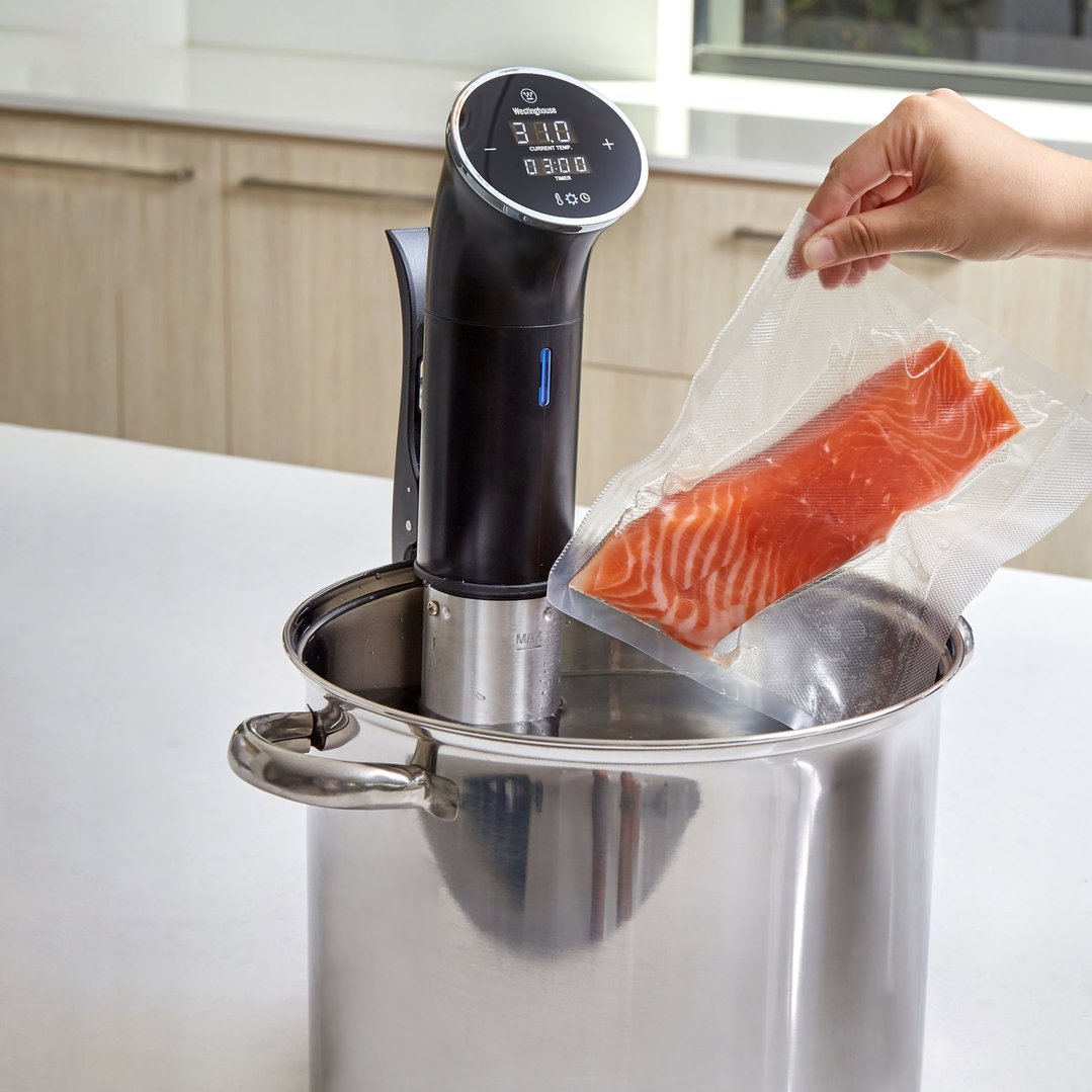 Hand placing a vacuum-sealed salmon fillet into a pot with a Sous Vide Immersion Cooker