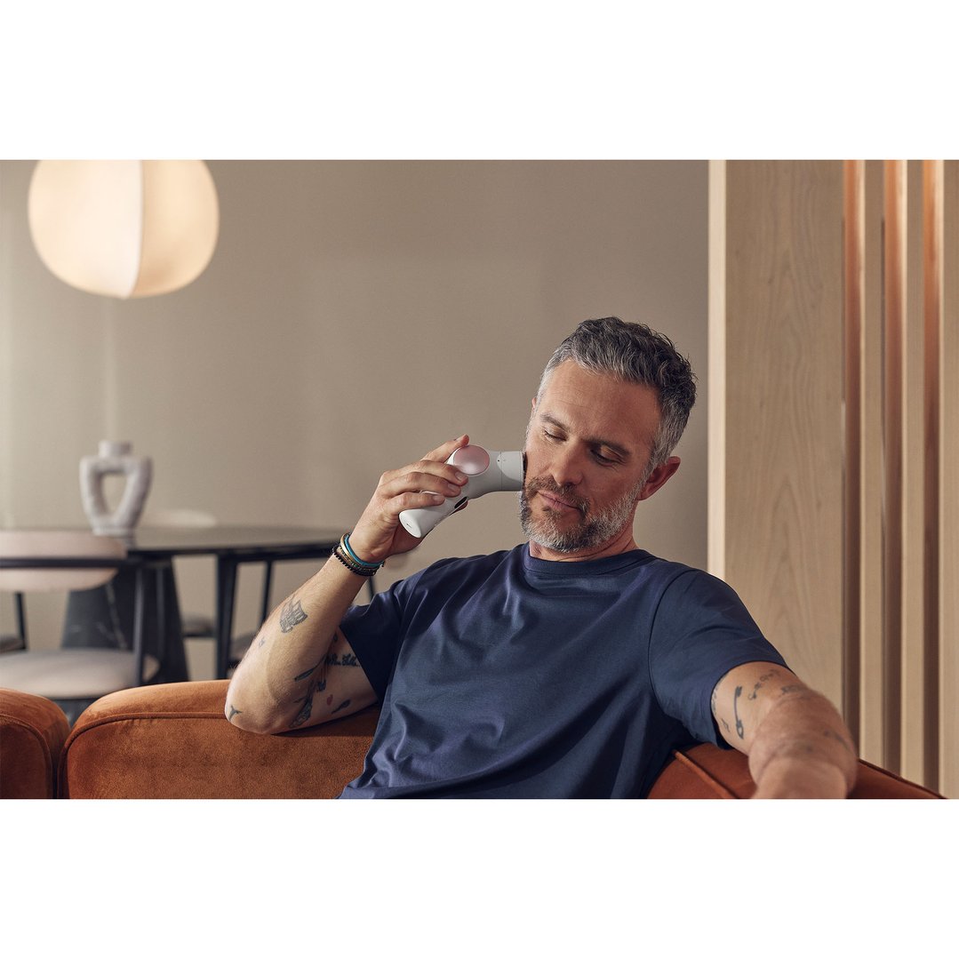 Man using a TheraFace PRO on his face while sitting on a sofa