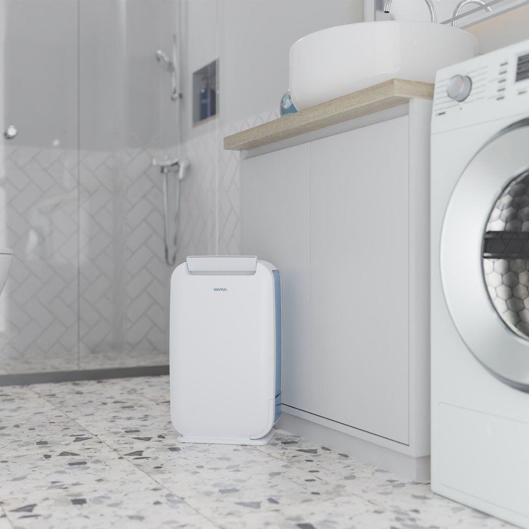 A white dehumidifier on a tiled floor in a modern bathroom next to a washing machine