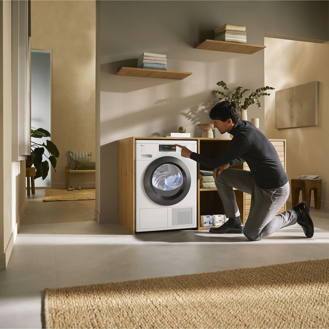 Man kneeling to operate a heat pump dryer in a laundry room