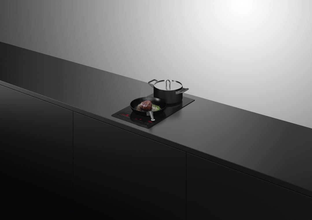 Black induction cooktop with a pan of steak and a pot on a dark counter
