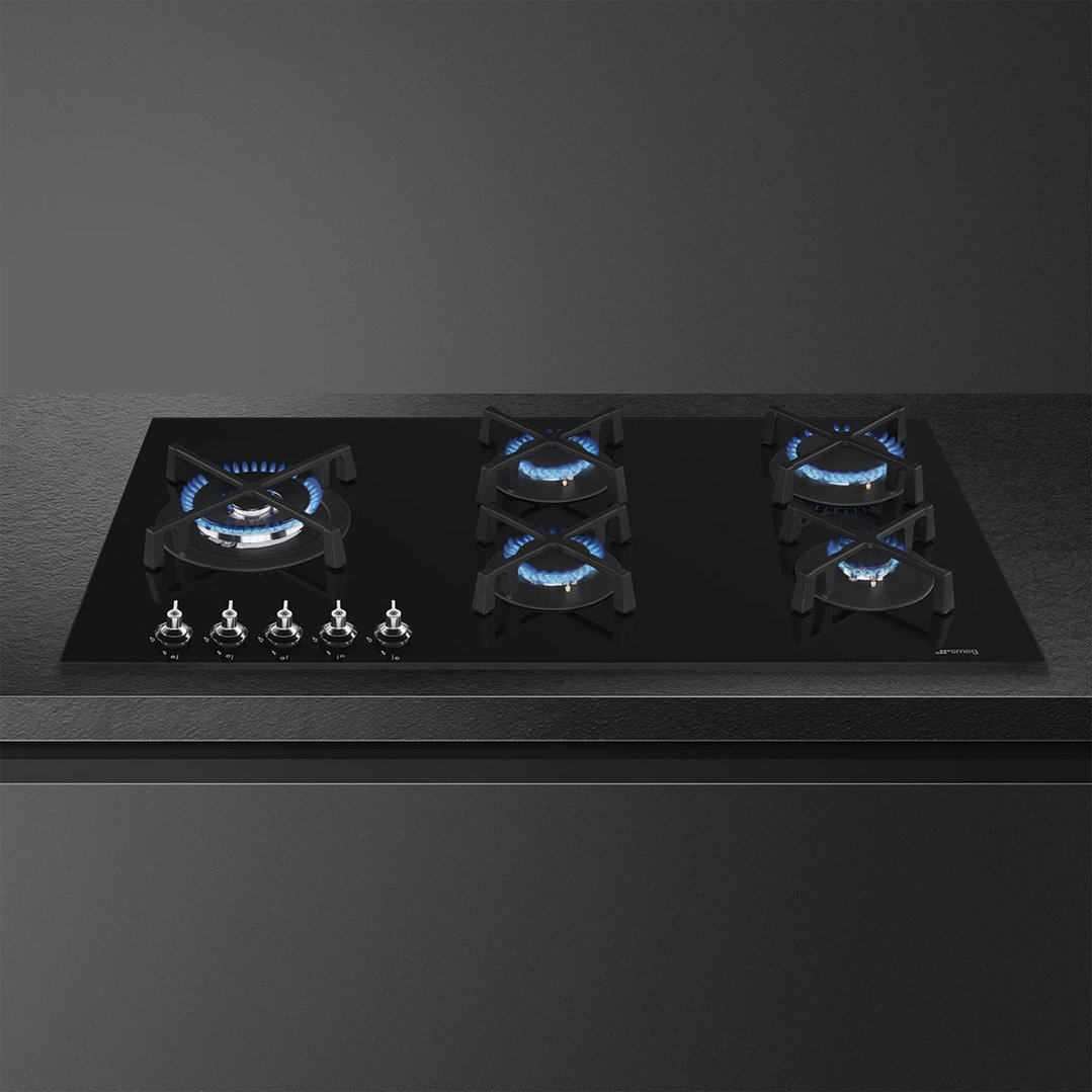 Black glass gas cooktop with five burners and controls on a dark countertop
