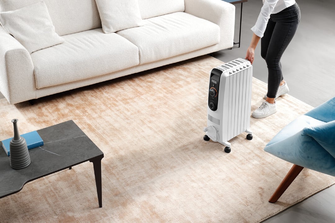 Woman moving a white oil column heater on wheels in a living room
