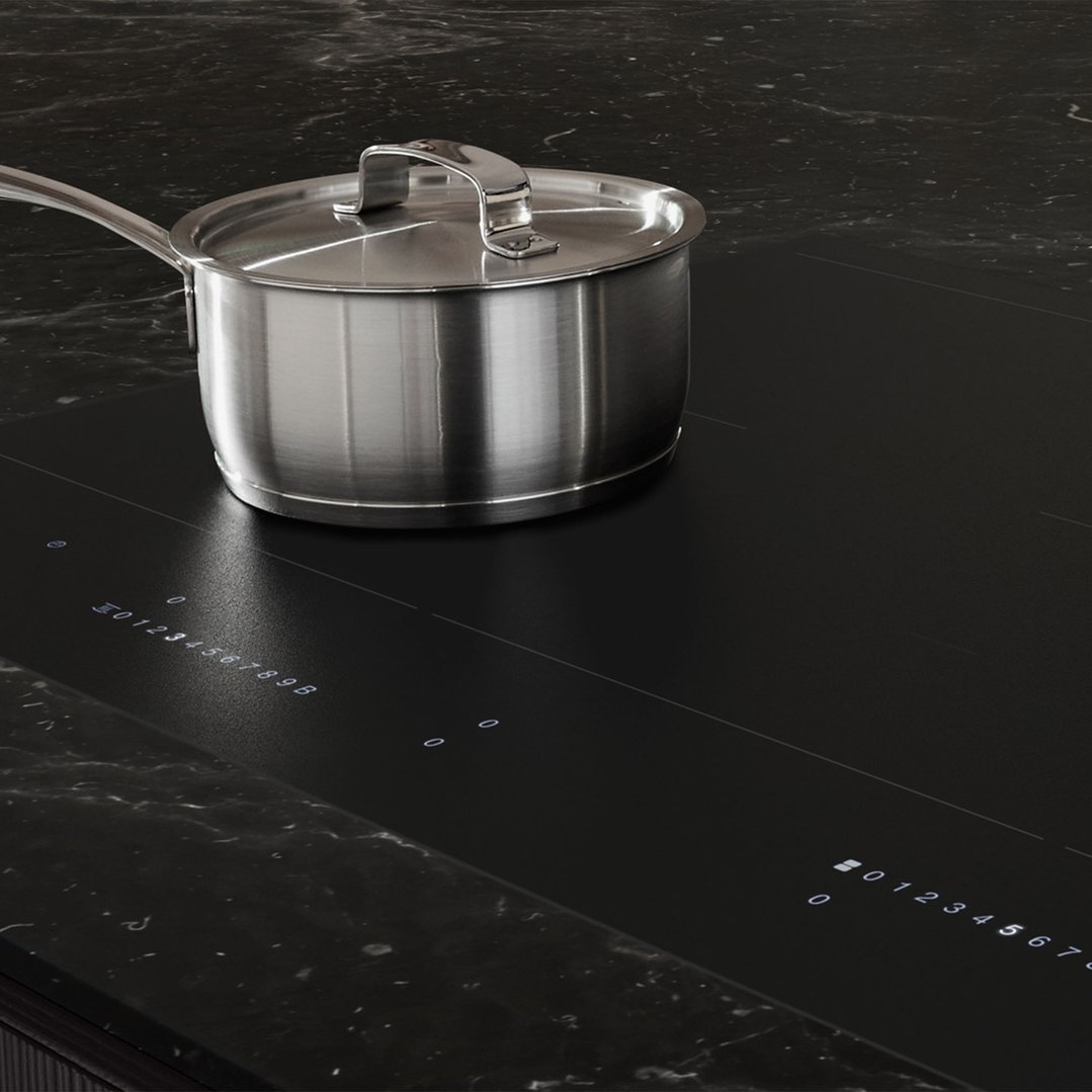 Stainless steel pot on a black induction cooktop in a dark kitchen