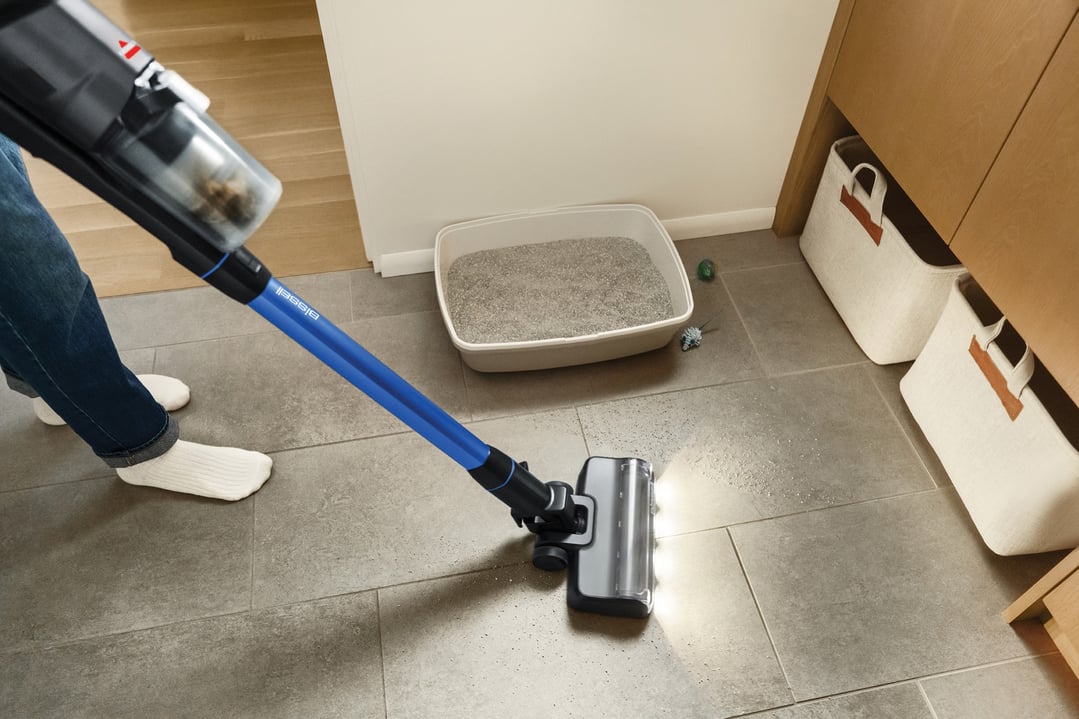 Person vacuuming a tiled floor with a BISSELL handstick vacuum near a cat litter box