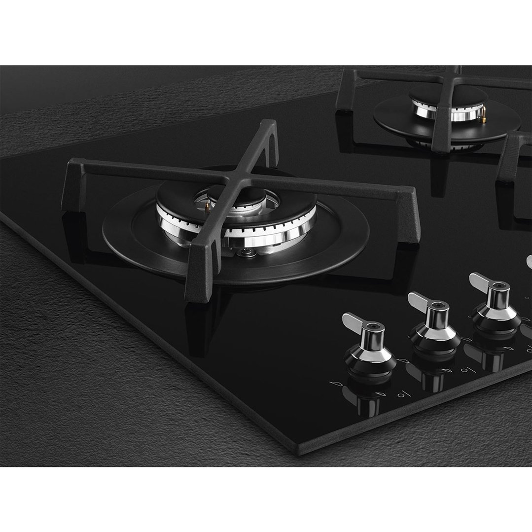 Close up of a black gas on glass cooktop with four burners and control knobs