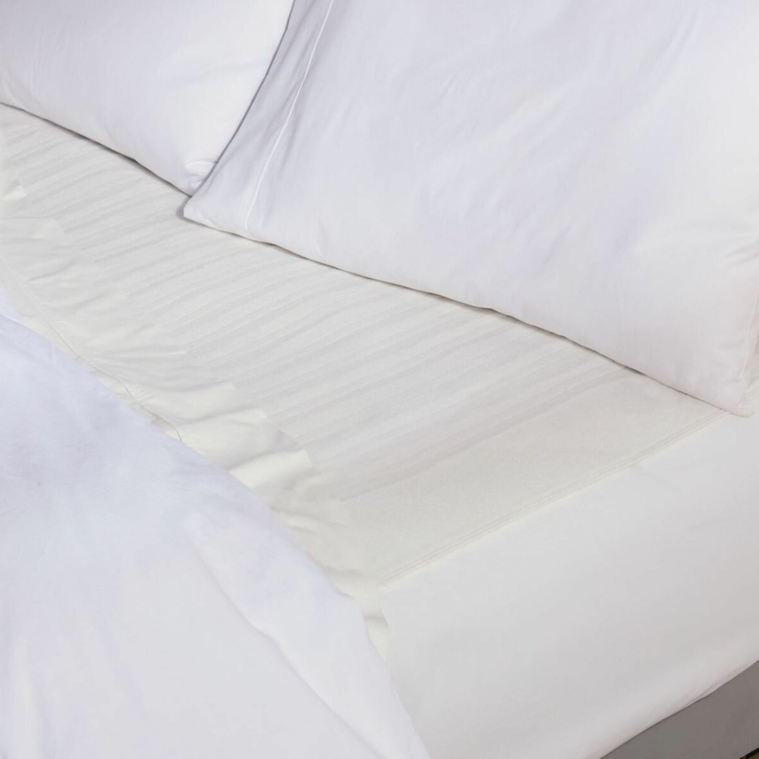 Close up of a white electric blanket on a bed with white pillows and sheets