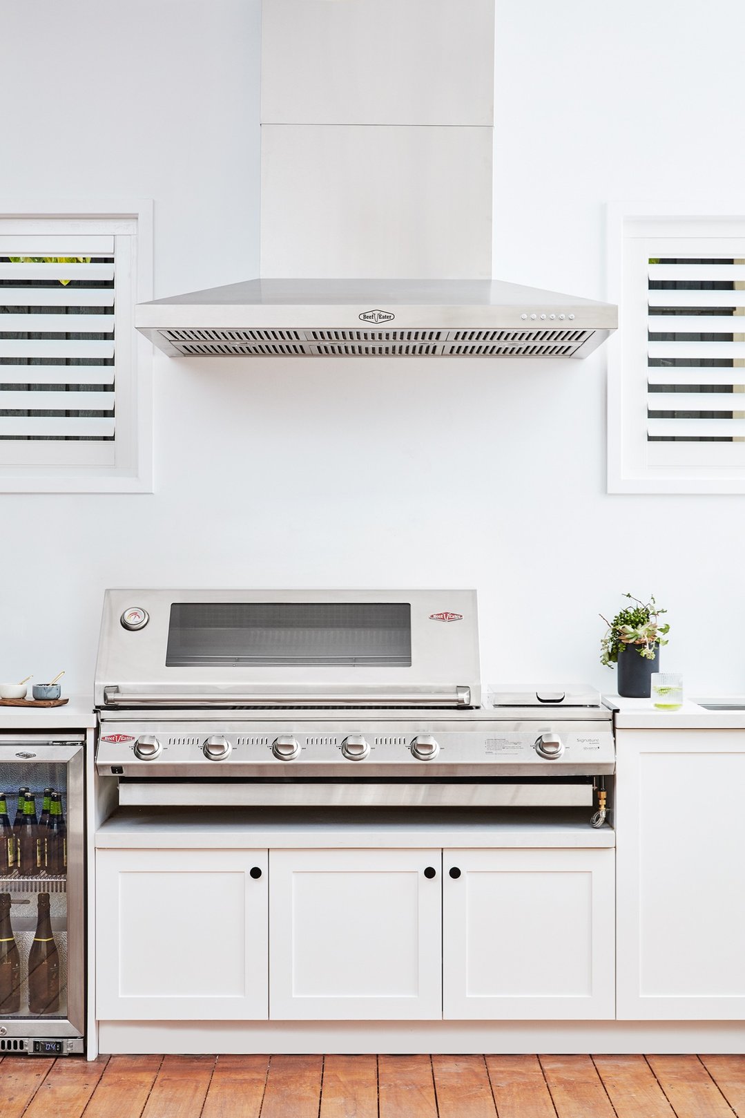 Stainless steel outdoor canopy hood mounted above a barbecue in an outdoor kitchen