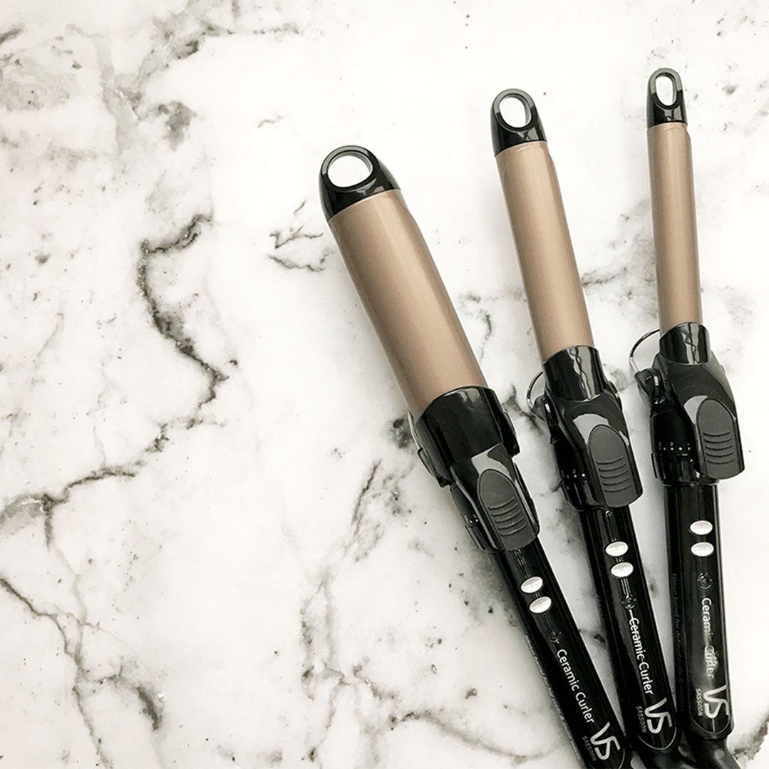 Three VS Sassoon ceramic curlers on a white marble surface