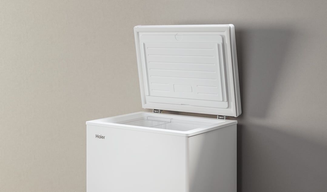 White Haier chest freezer with the lid open against a neutral wall