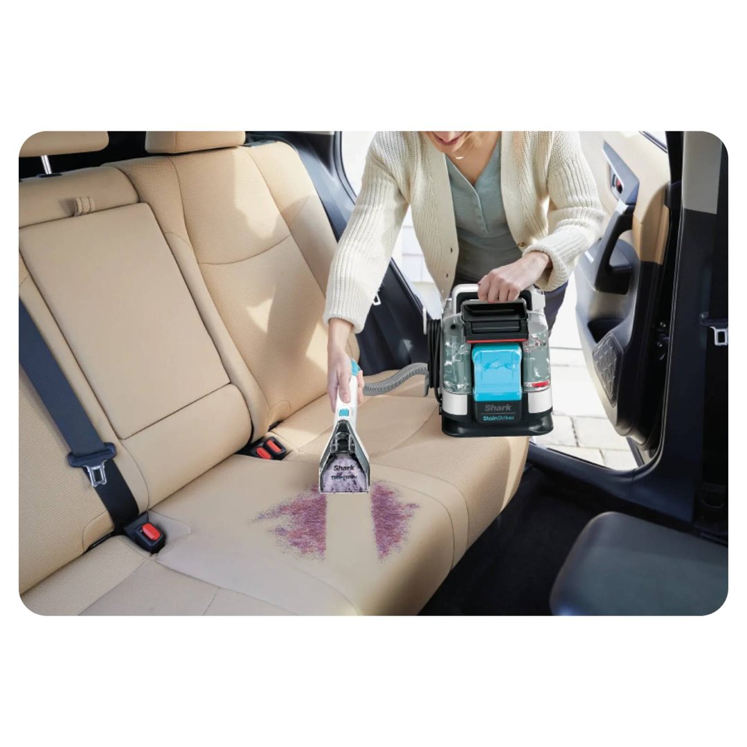 Woman cleaning a car seat with a portable spot cleaner, removing a red stain