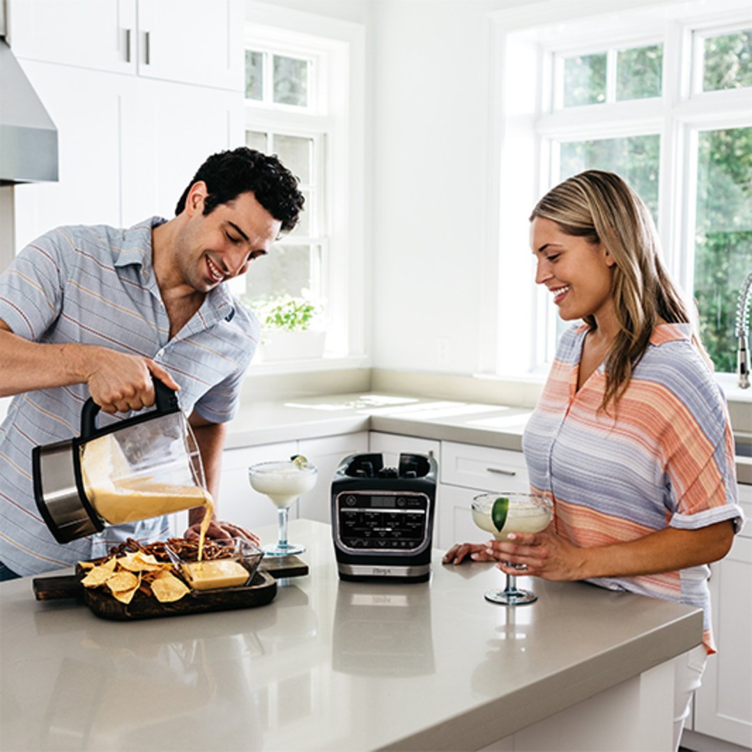 Man pouring from a blender into a bowl with a woman smiling nearby