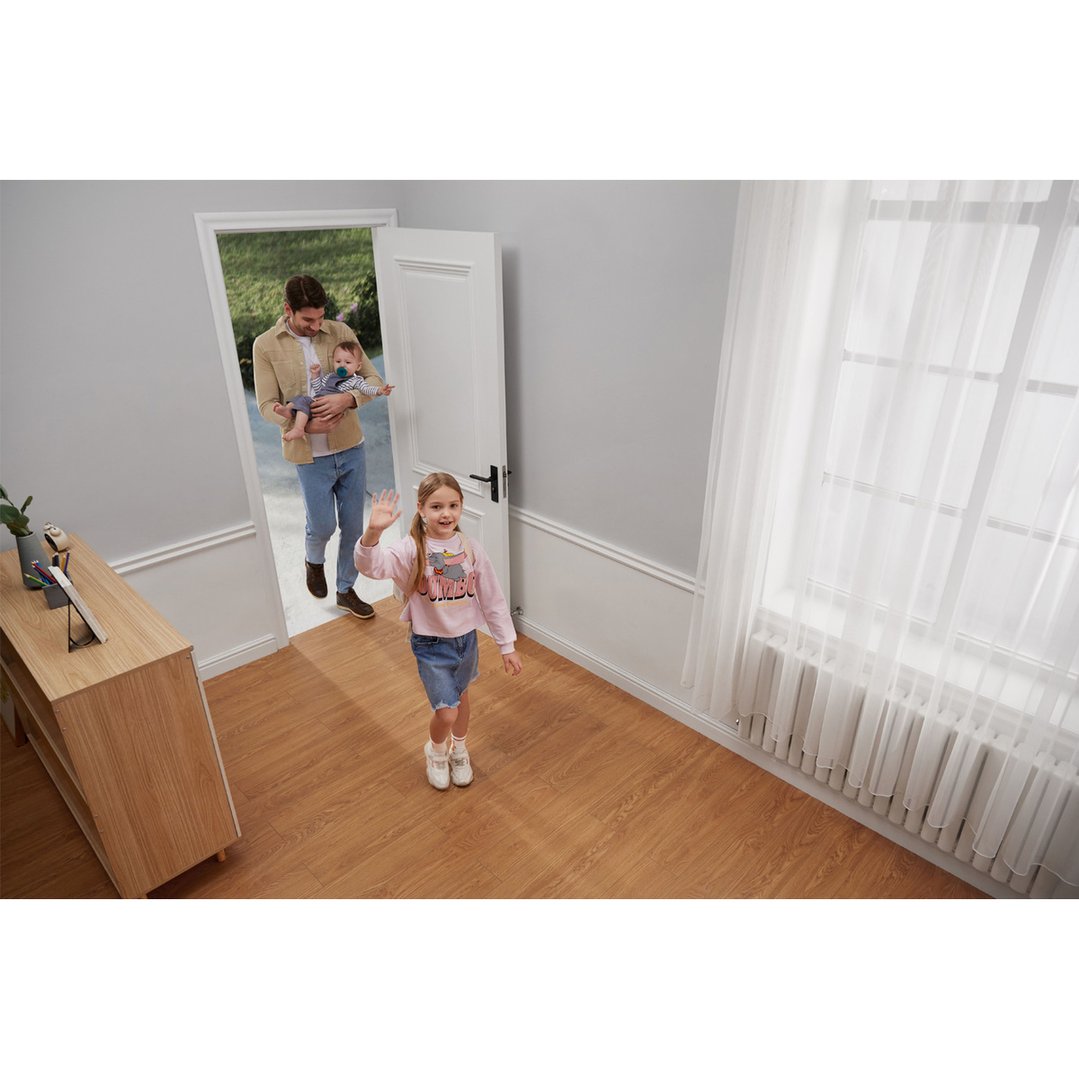 A security camera observing a girl waving and a man holding a baby entering a room