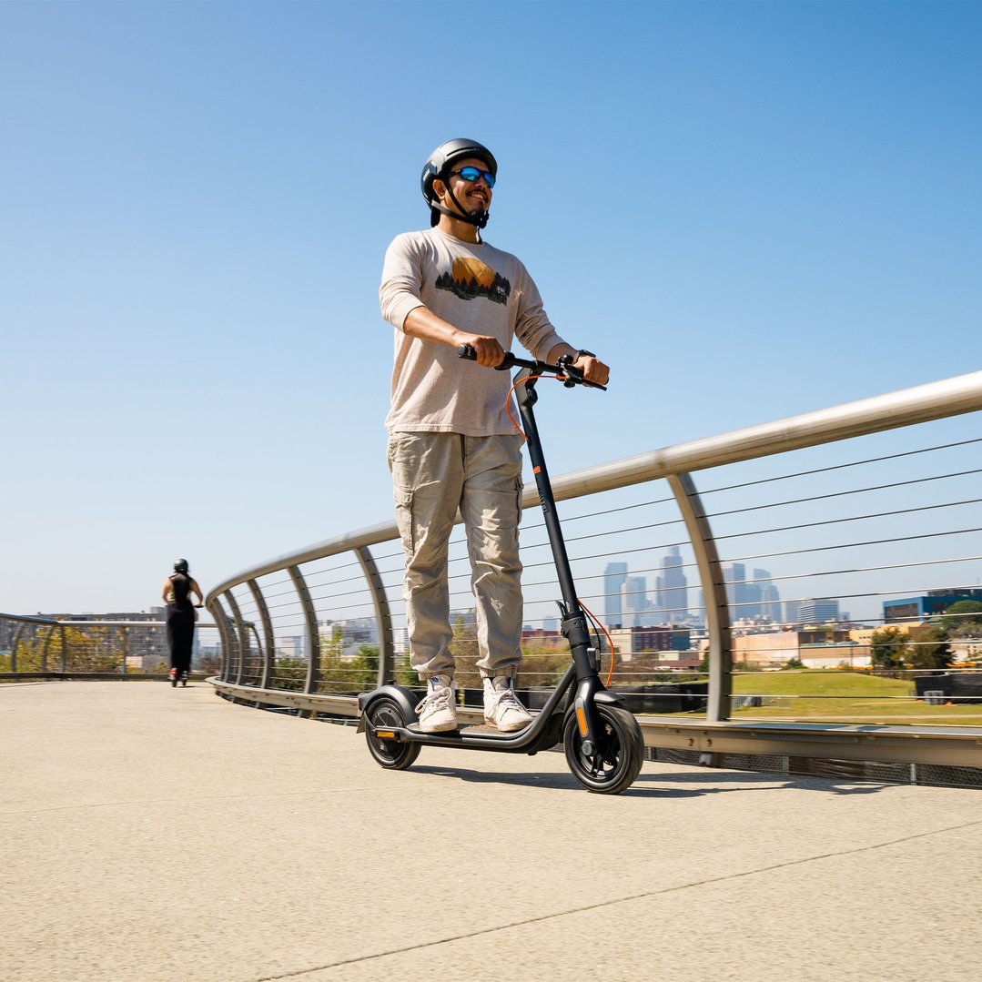 Man riding an electric scooter on a bridge with city skyline