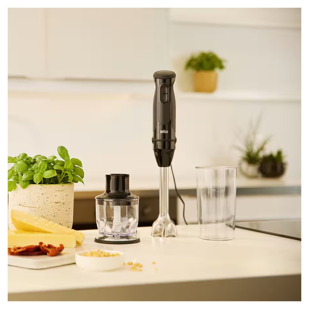 Black hand blender and accessories on a kitchen counter with food ingredients