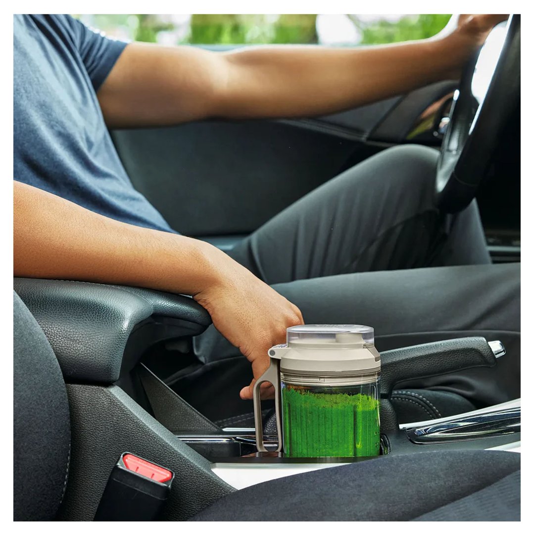 Person holding a Ninja Blast portable blender with green contents in a car