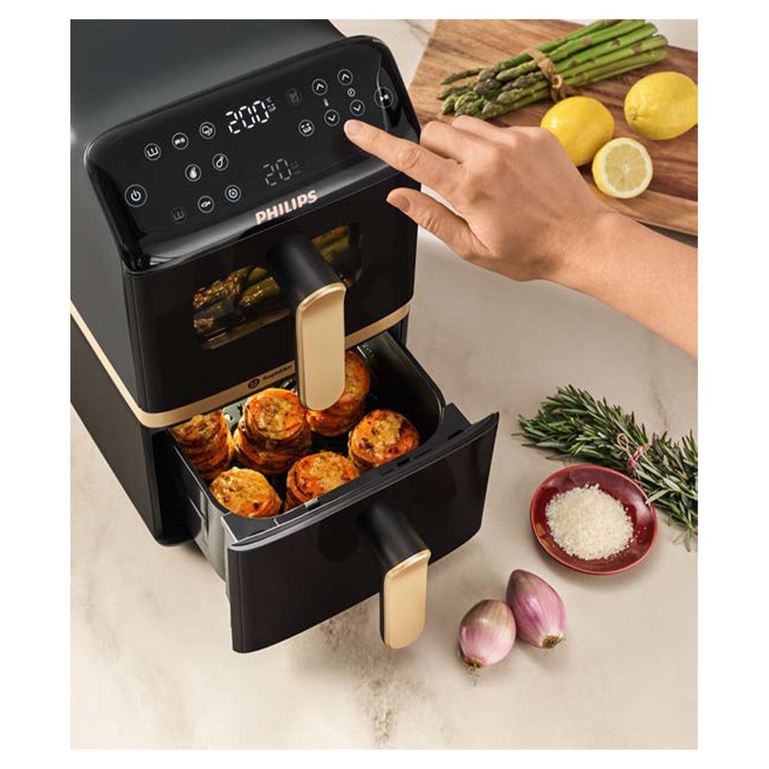 Hand adjusting settings on a Philips Airfryer with food and ingredients nearby