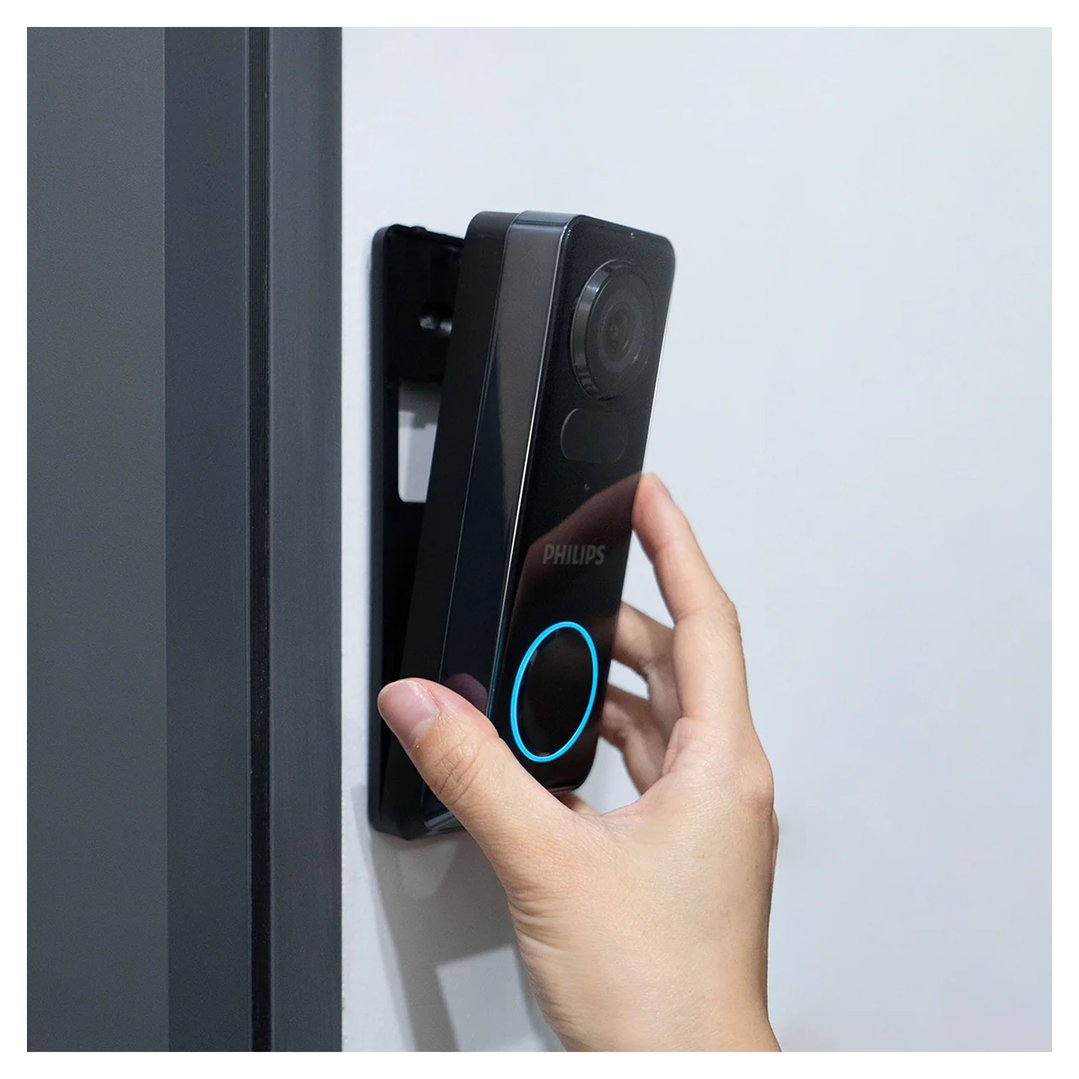 Hand interacting with a black Philips video doorbell on a white wall