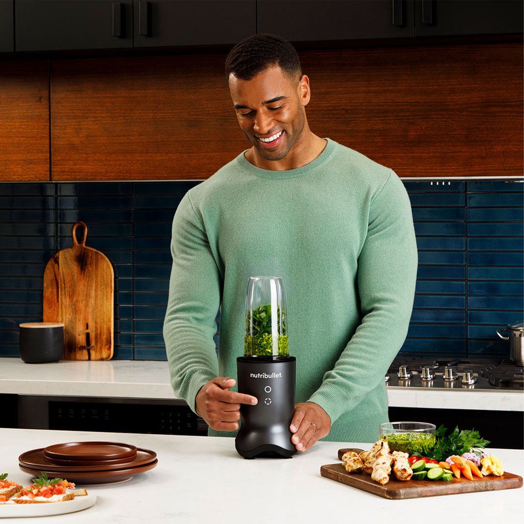Man blending green ingredients in a NUTRiBULLET blender on a kitchen counter
