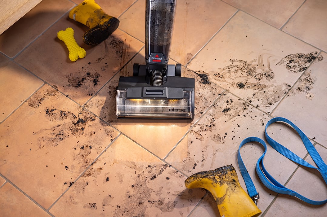 handStickVacuum cleaning muddy paw prints on a tiled floor with dog accessories