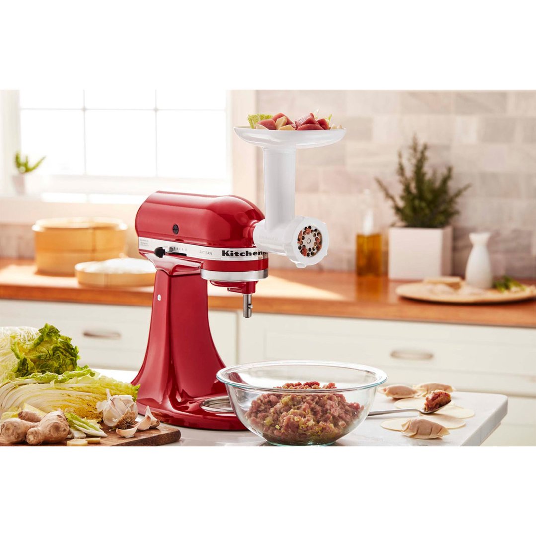 Red stand mixer with food grinder attachment in a kitchen setting