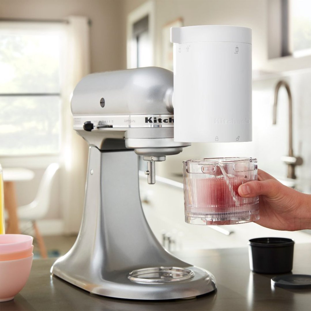 Hand holding a container of shave ice attachment under a stand mixer