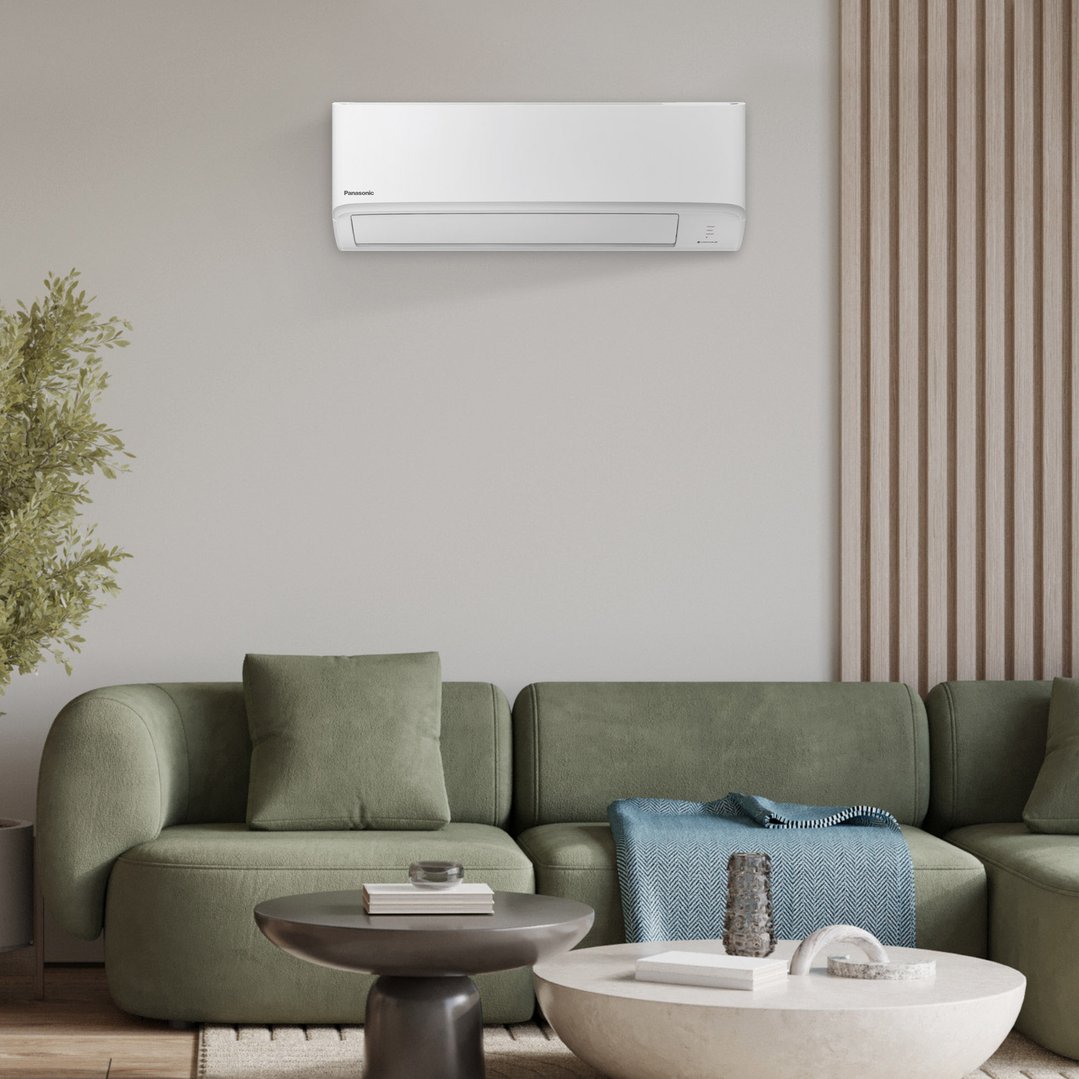 Panasonic air conditioner mounted on a wall above a green sofa in a living room