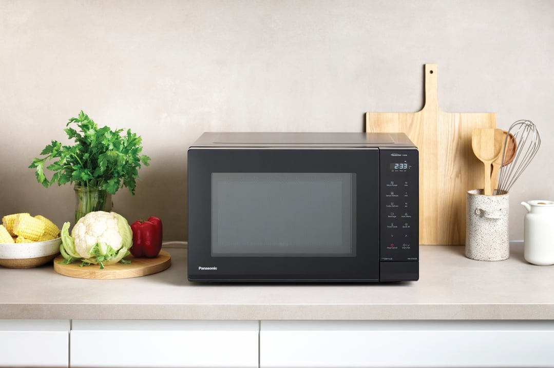 Black Panasonic microwave on a kitchen counter with vegetables and kitchen utensils