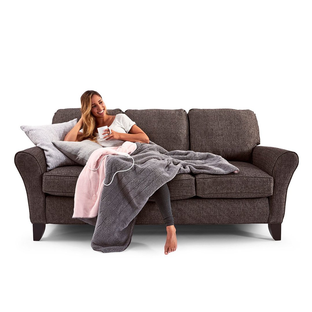 Woman relaxing on a sofa with a grey and pink electric blanket and a mug