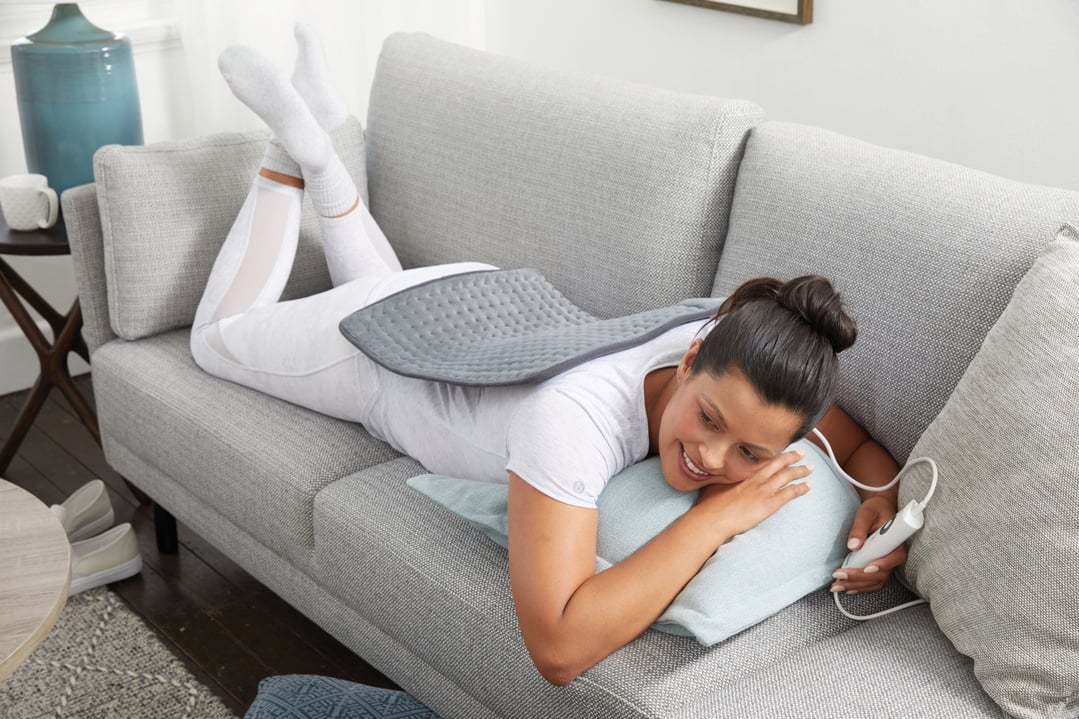Woman lying on a couch with a heating pad on her back