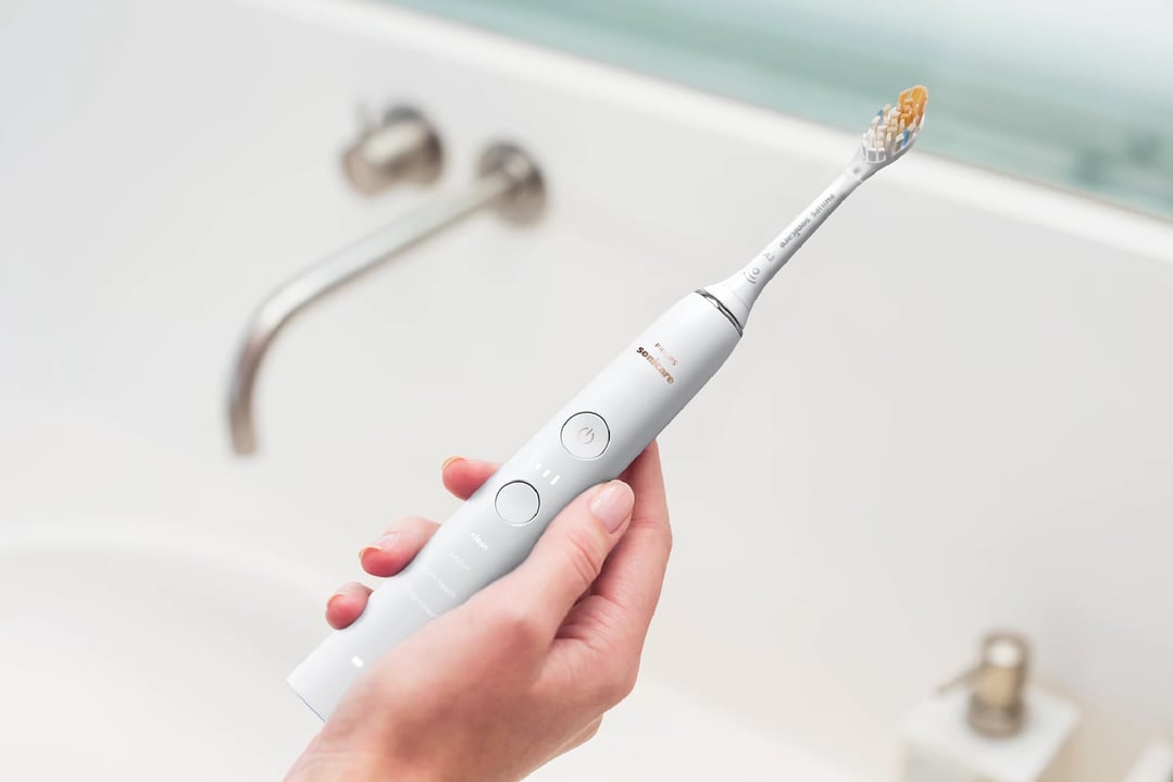 Hand holding a white Philips Sonicare electric toothbrush over a bathroom sink