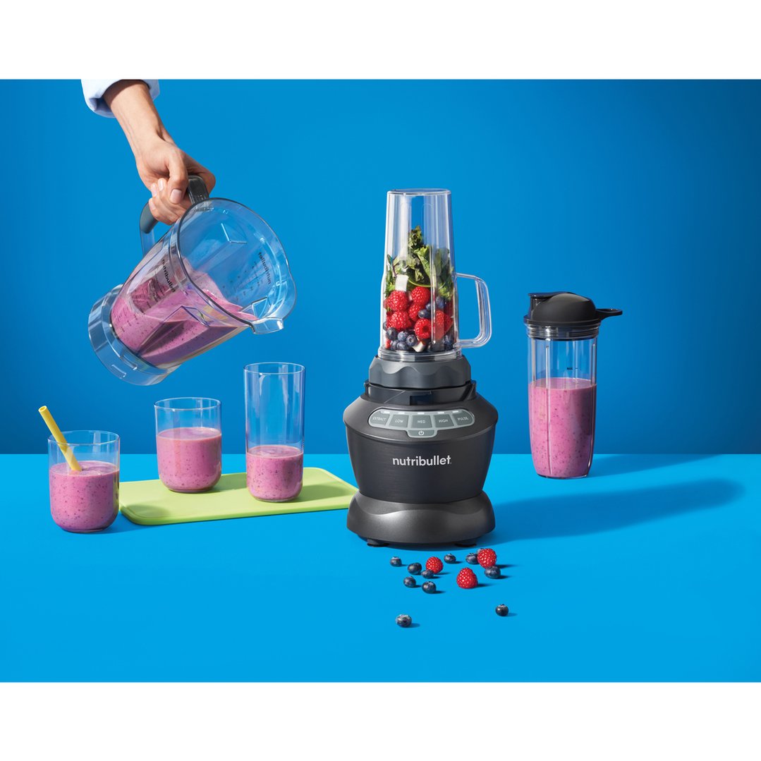 Hand pouring smoothie from a blender into glasses on a blue surface