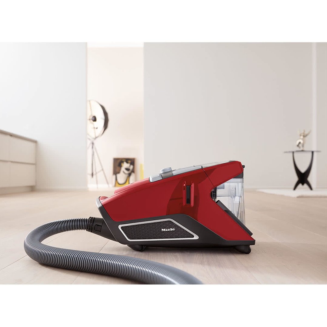 Red Miele Blizzard CX1 bagless vacuum cleaner on a wooden floor in a living room