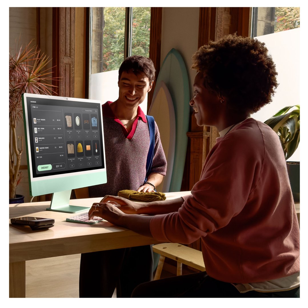 Two people interacting with an APPLE iMac desktopAllInOneComputers on a wooden table