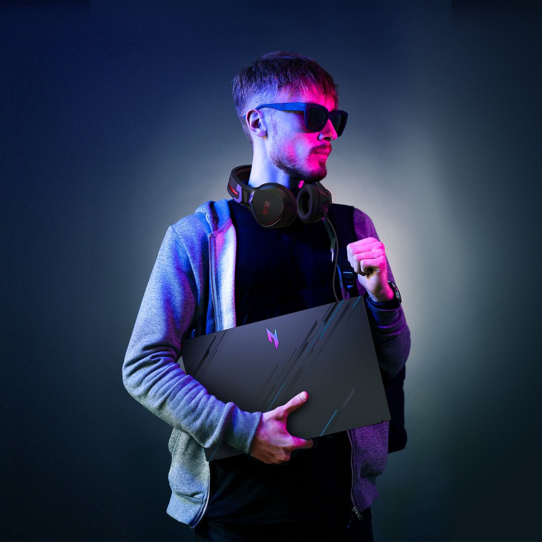 Man in sunglasses and headphones holding a laptop in a dark, colorful setting