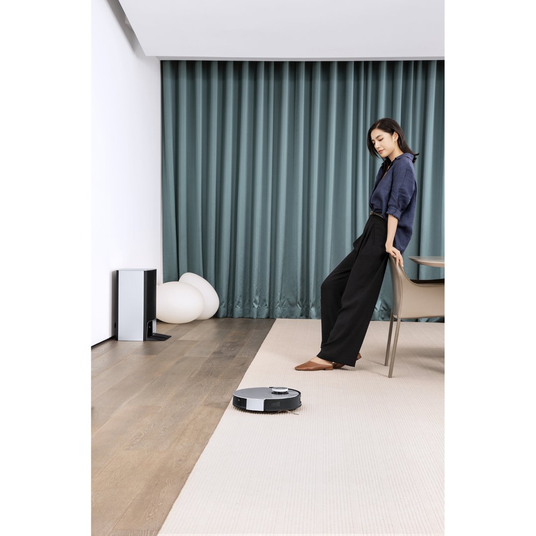 Woman leaning on a chair while a DEEBOT X1 OMNI robotic vacuum cleans the floor